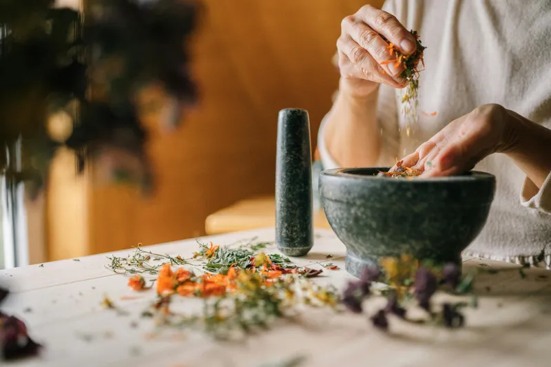 A person crafting a natural remedy by mixing dried herbs and mineral salts, highlighting holistic health and plant-based self-care.