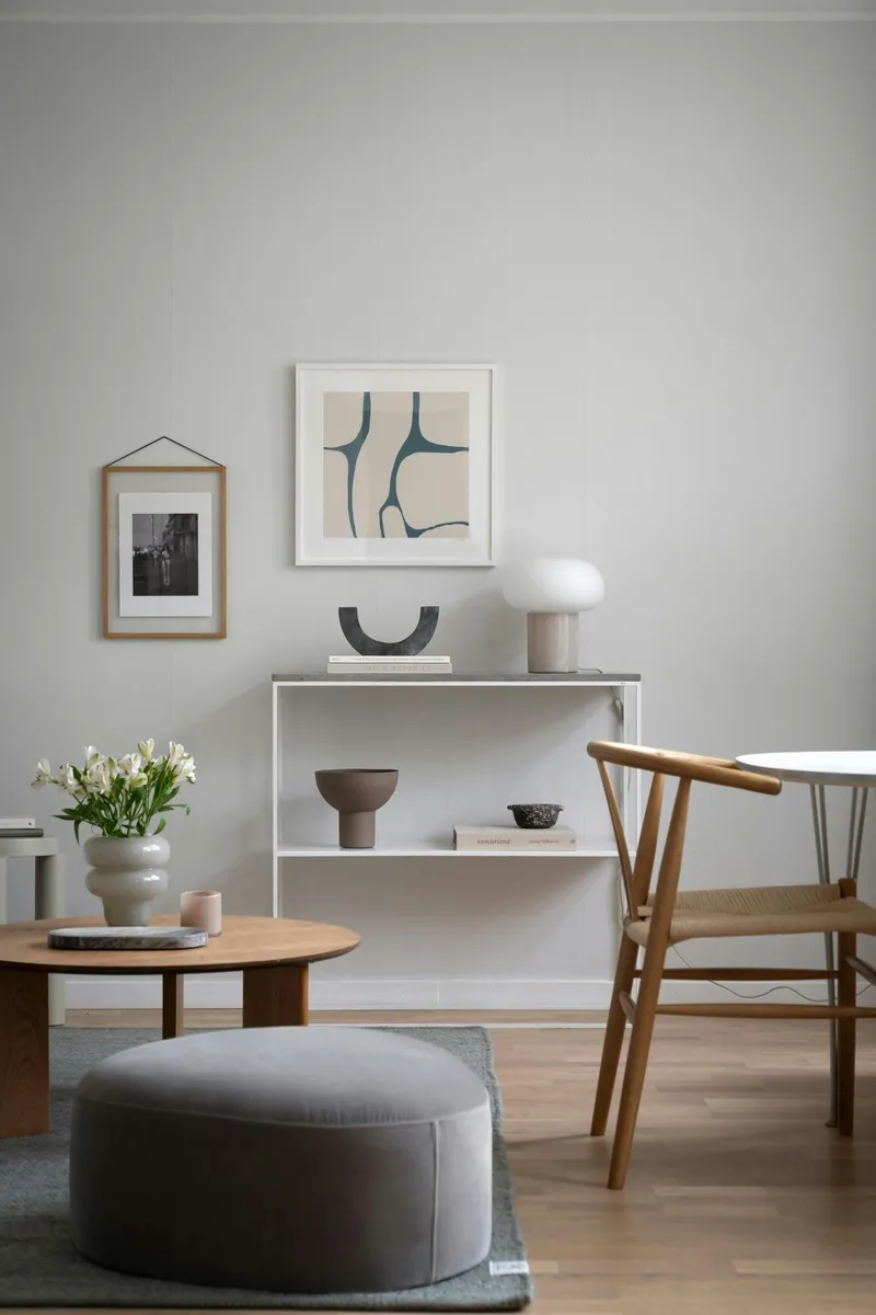 Minimalist living room with framed artwork, modern lamp, and decorative vases on a white shelf.